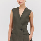 A woman modeling a sleeveless, single-breasted, mid-length Liquorice Wool Ellipsis Vest with functional front pockets, in a gray color.