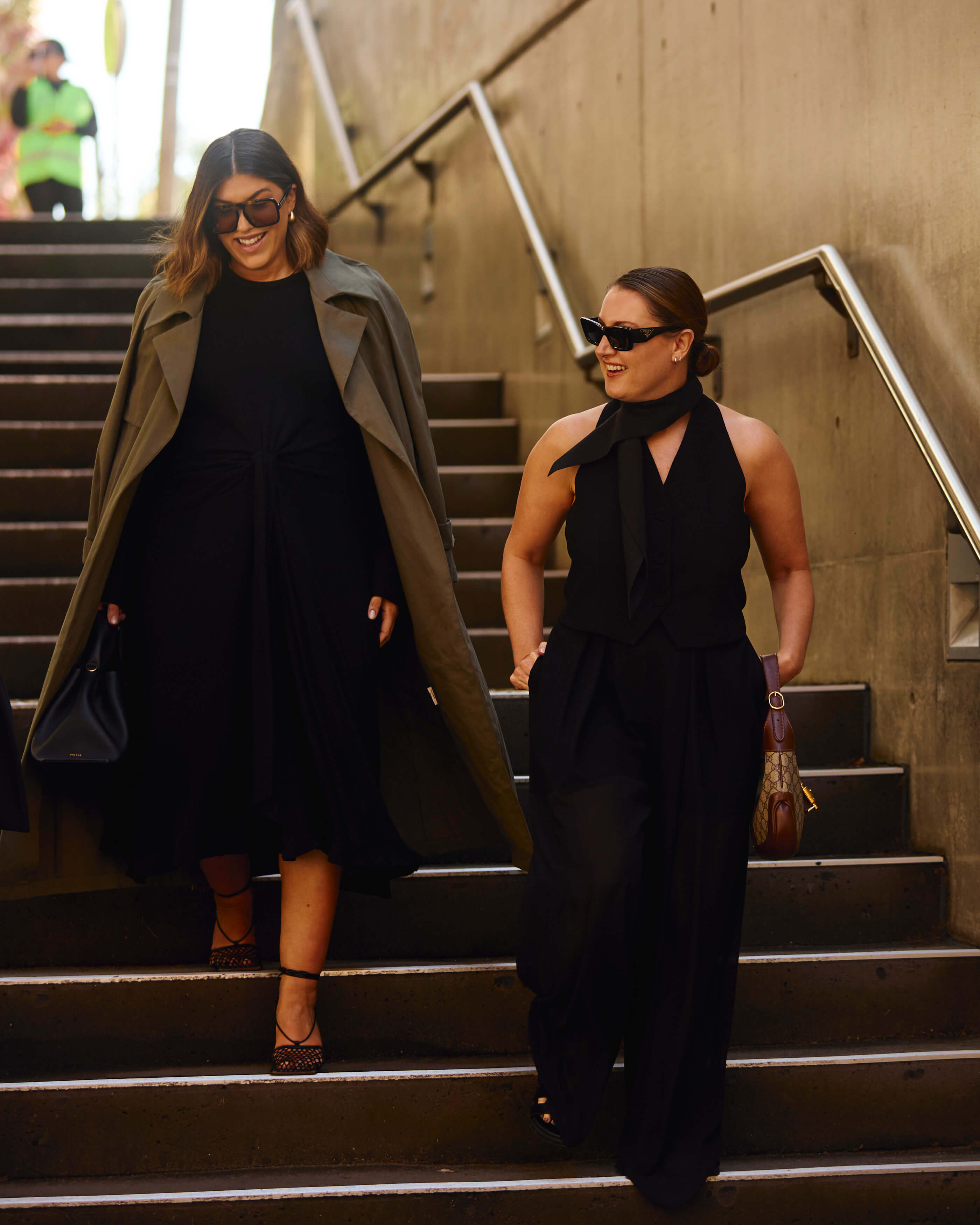 Bec and Marissa Karagiorgos wear the Olive Crepe Composition Jacket, Mori Mini Dress, Khaki Twill Henri Trench and Black Jersey Figurative Dress from Bianca Spender at Sydney's Carriageworks 