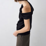 A model shown from the side and back wearing a black off-the-shoulder knit top and dark olive trousers, set against a plain light gray studio background.