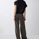 A model shown from the back wearing a black draped short-sleeve top and wide-leg olive brown trousers, standing against a light gray studio background.