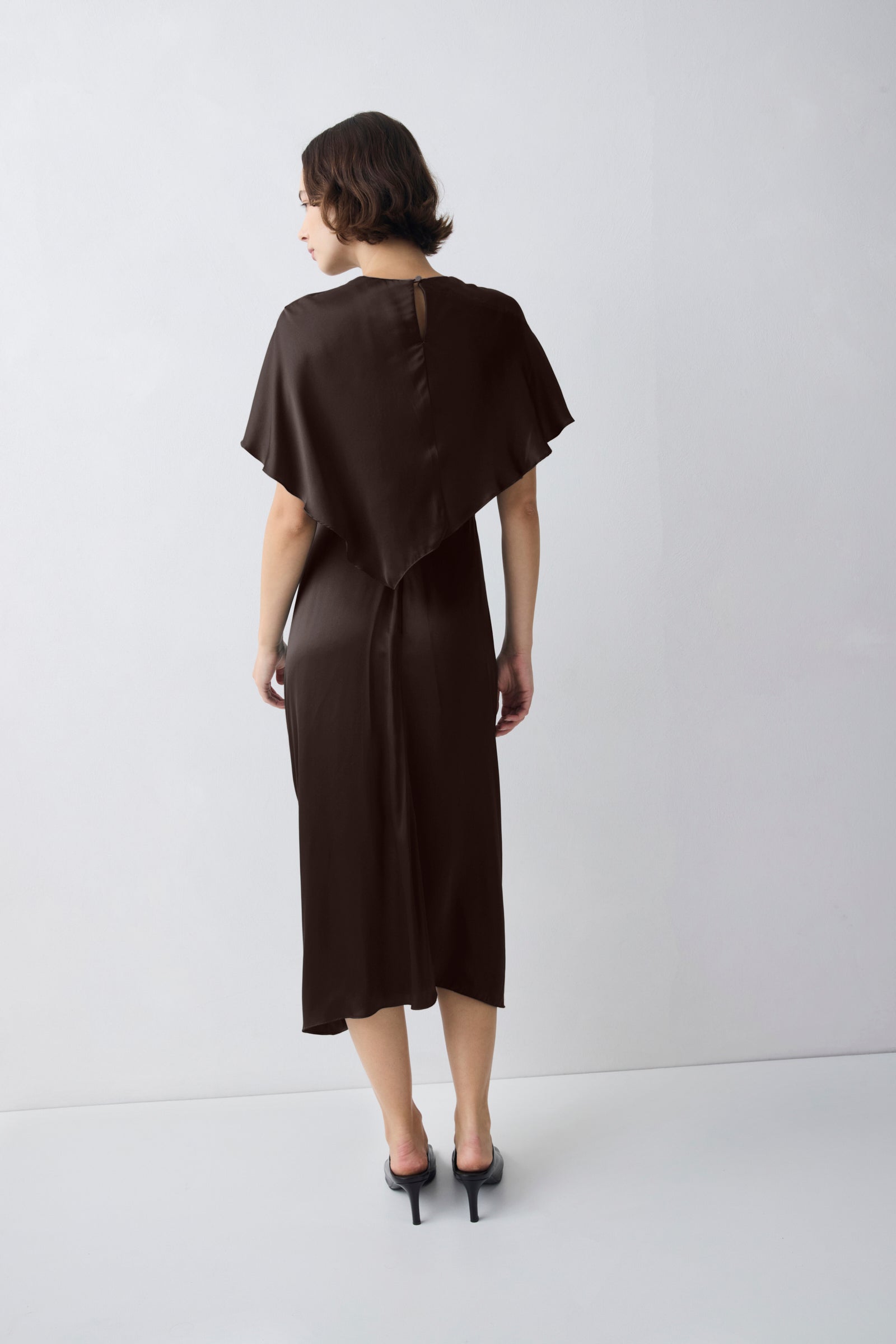 Woman wearing a brown dress with a cape-like feature on a white background