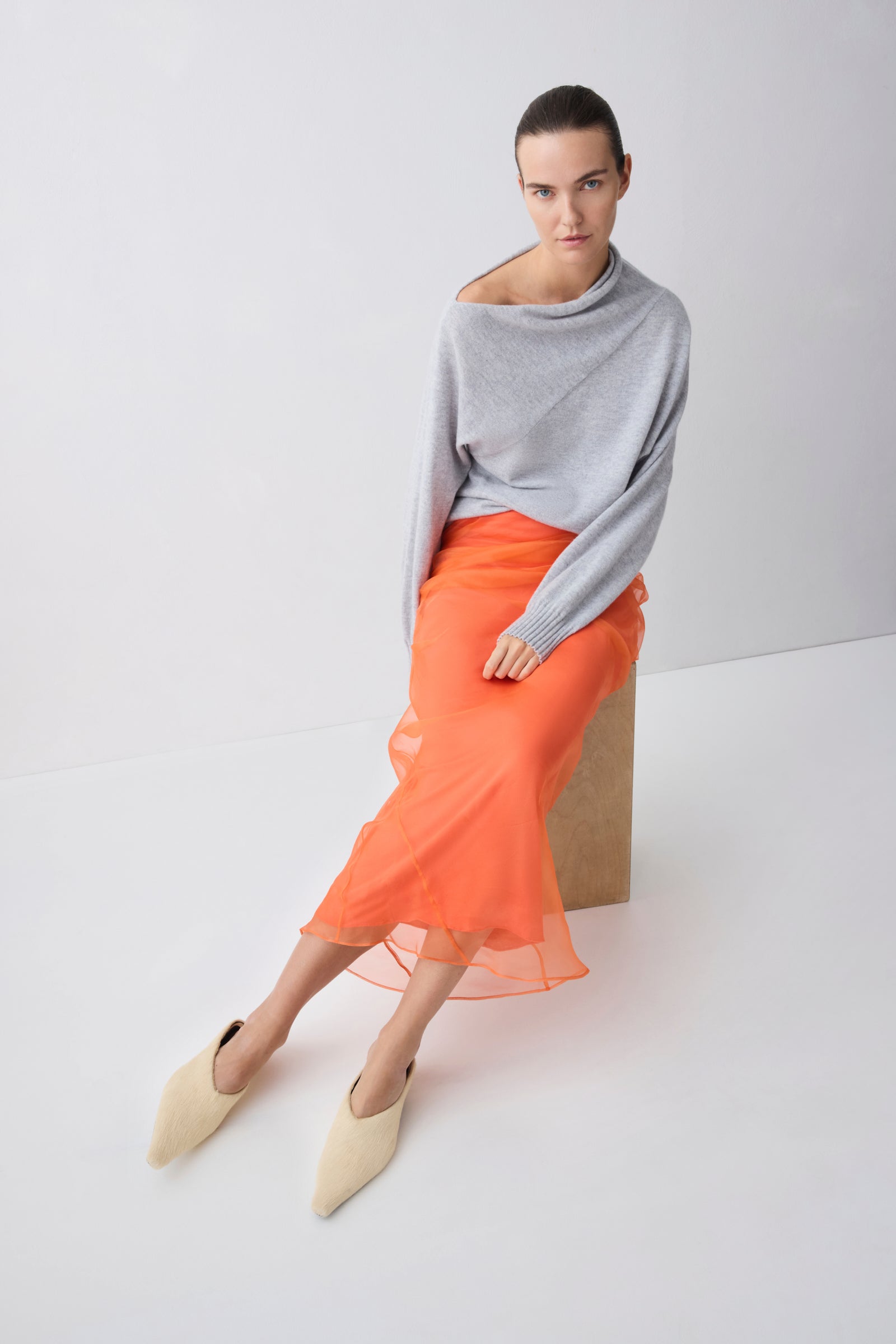 Woman wearing a gray sweater and orange skirt on a white background