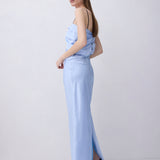 A woman modeling a light blue strapless maxi dress with a side slit, paired with black heels, standing against a plain light gray studio background.