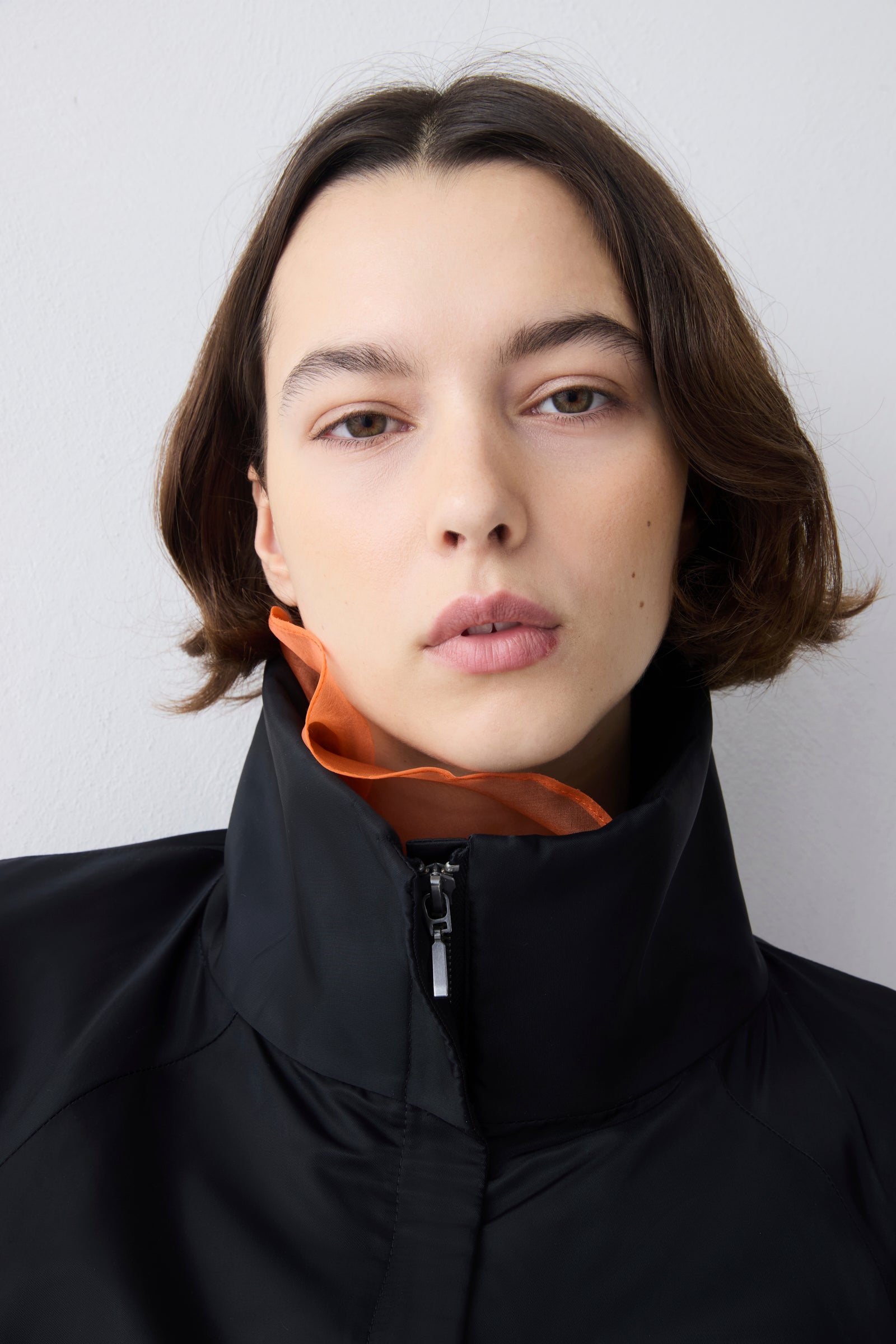 Person wearing a black jacket with an orange collar against a white background