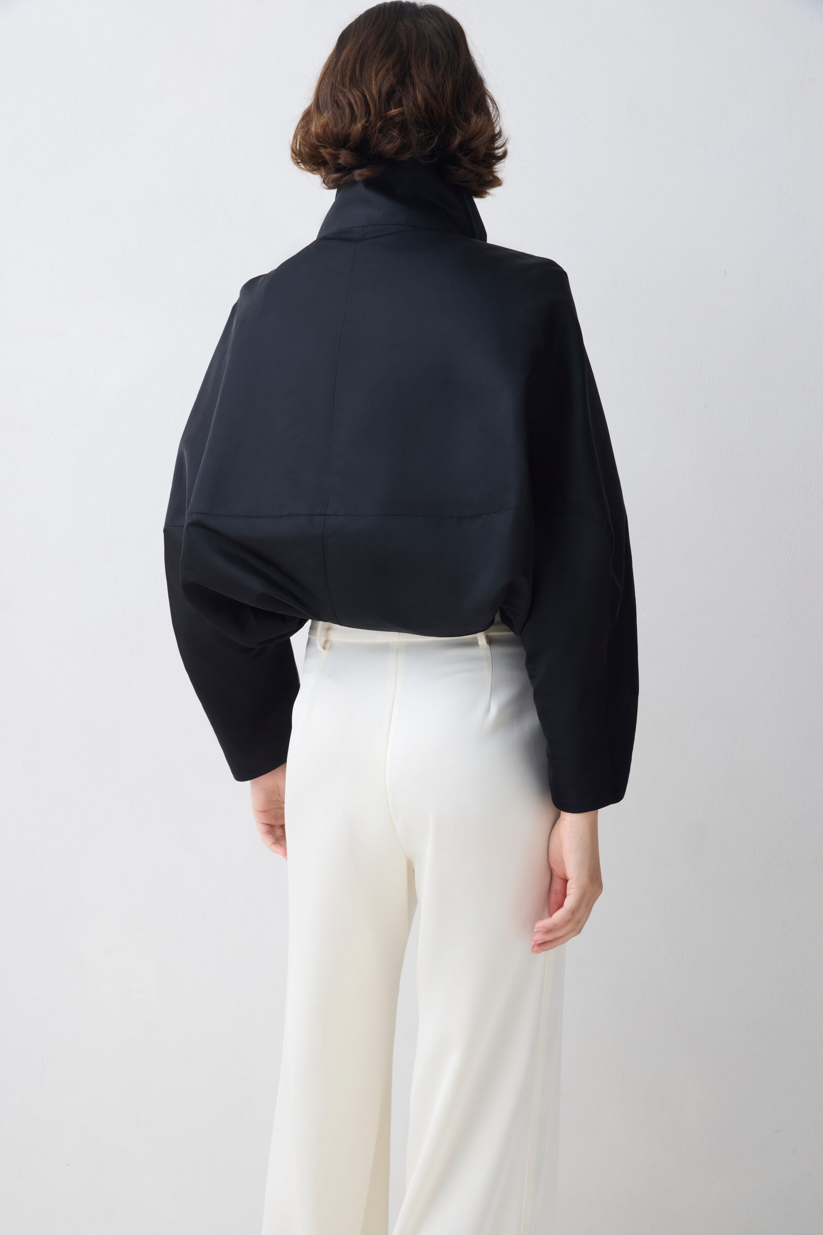 Person wearing a black shirt and white pants on a plain background