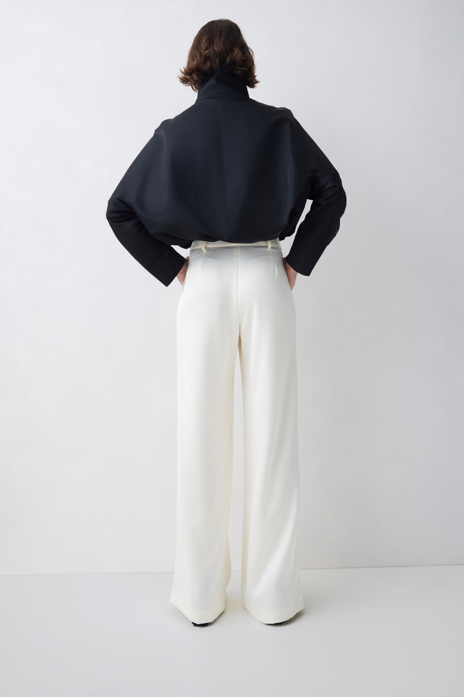 Person wearing a black jacket and white pants on a white background