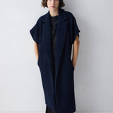 Person wearing a long navy blue coat against a white background