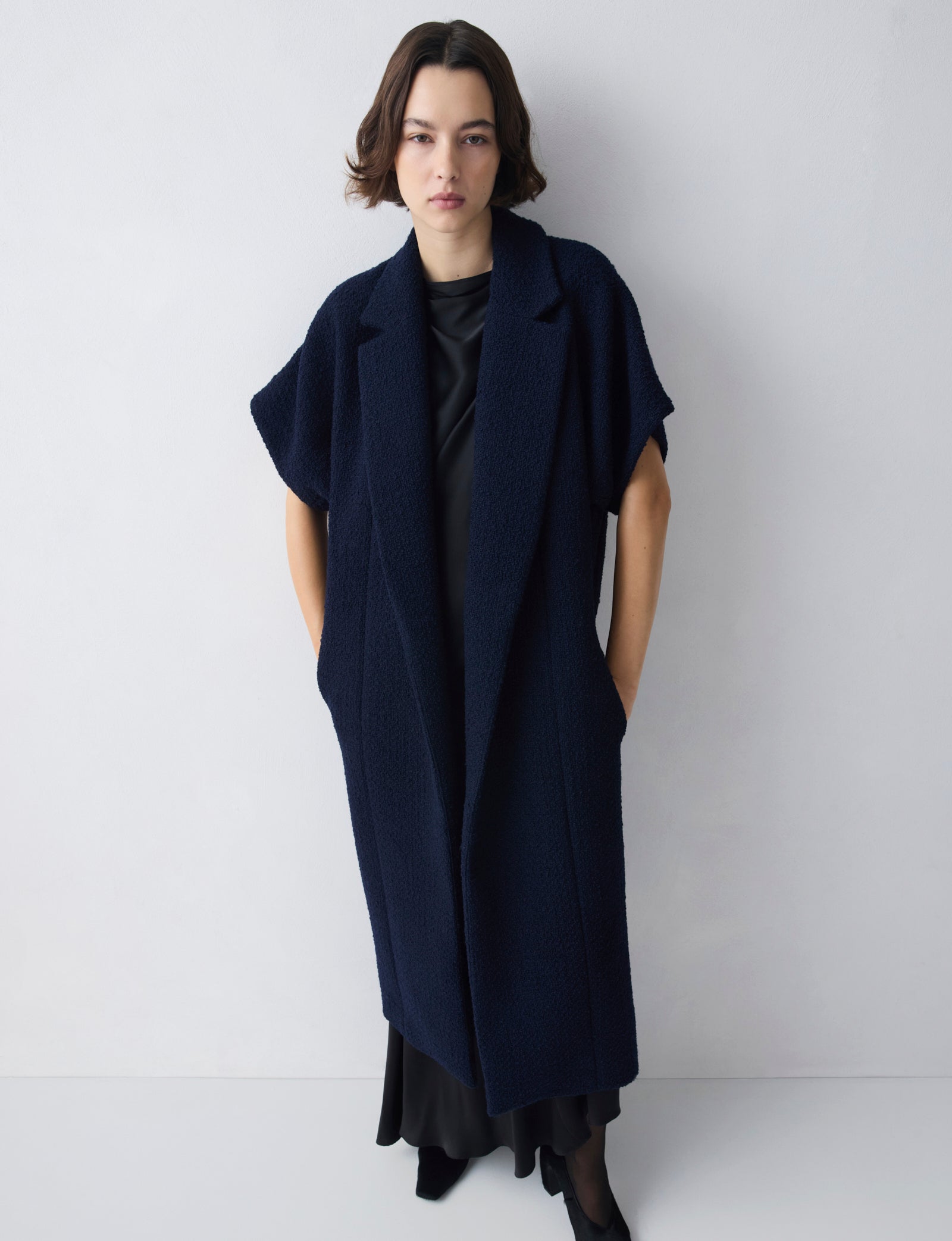 Person wearing a long navy blue coat against a white background