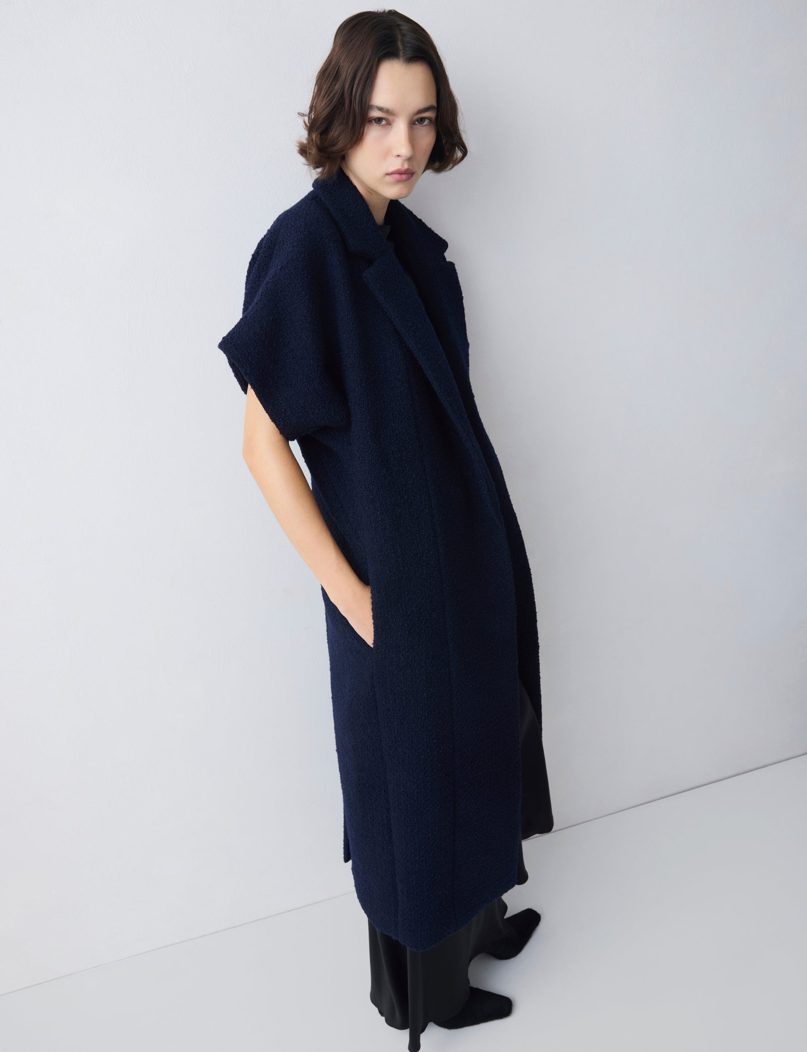 Person wearing a long dark blue coat against a white background