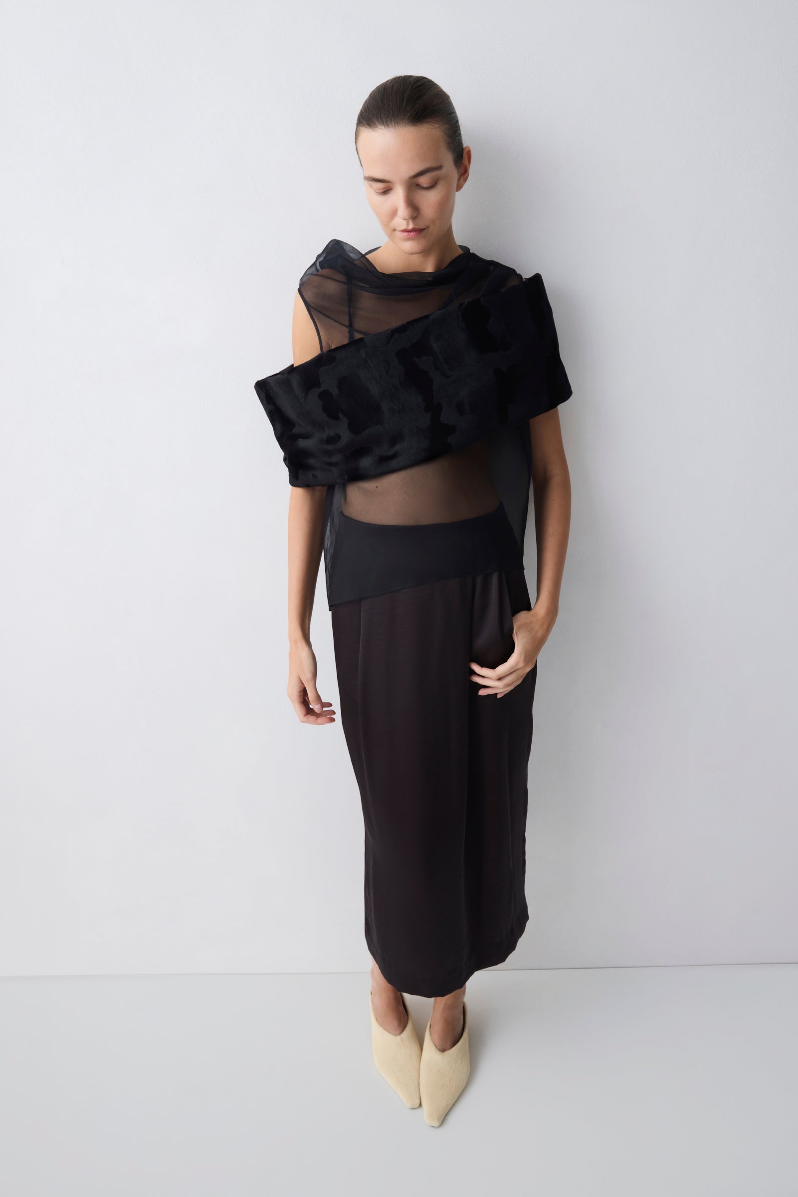 Woman wearing a black outfit with sheer top against a white background