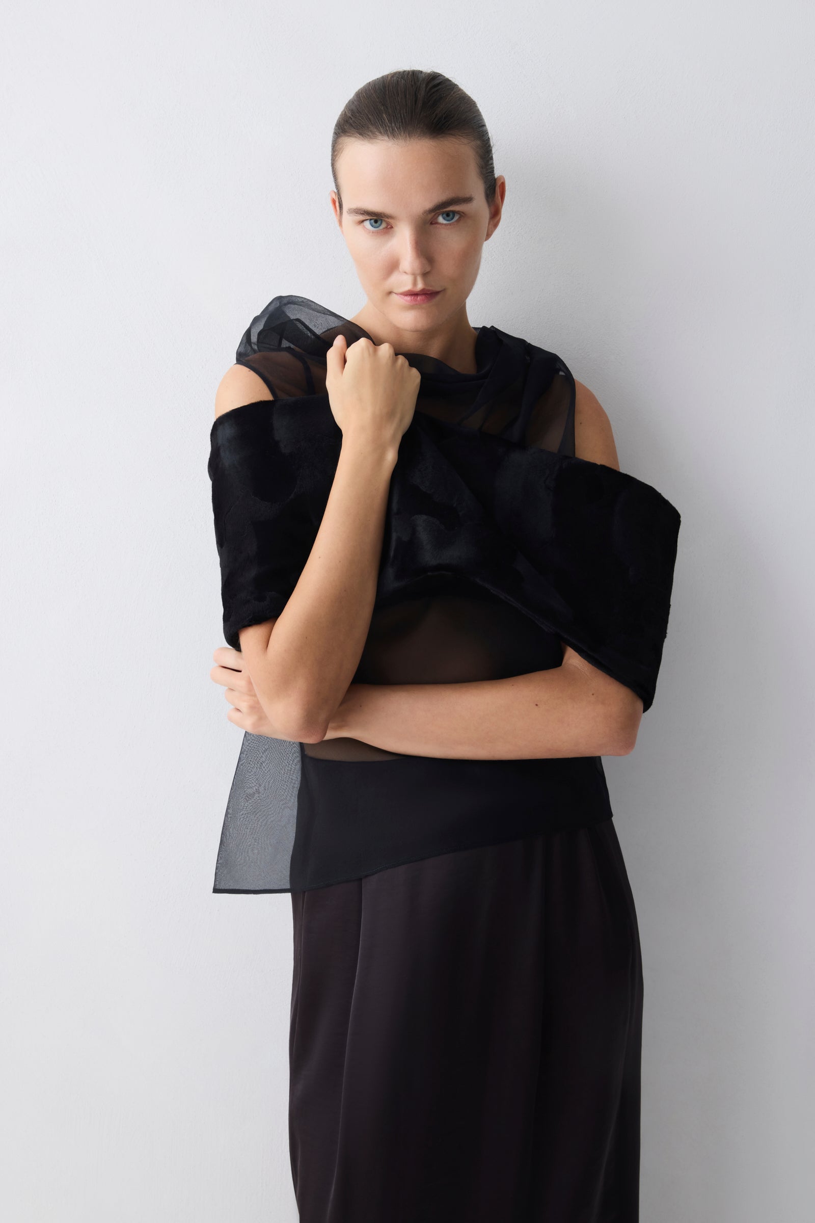 Woman wearing a black outfit with sheer sleeves against a white background