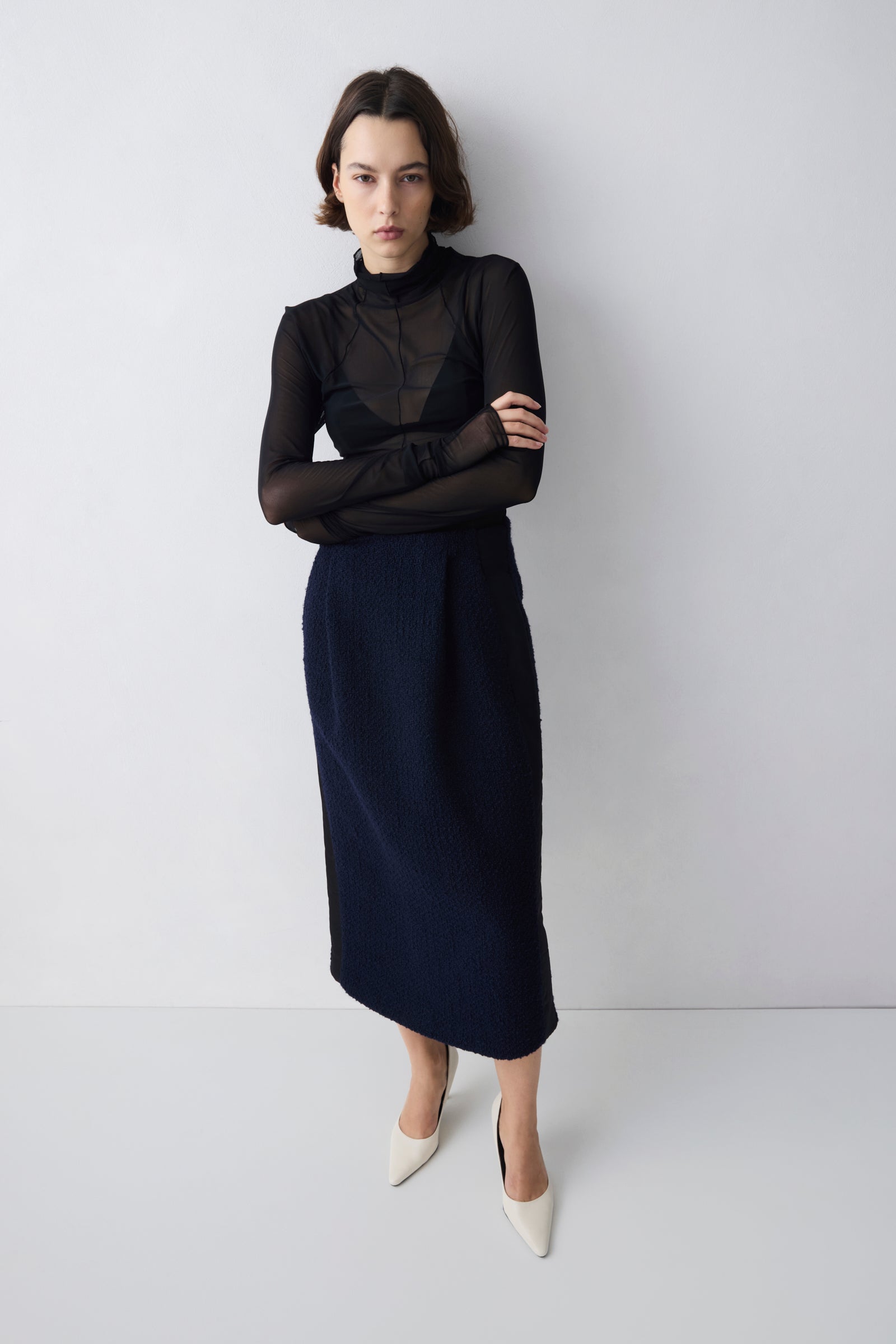 Woman wearing a black top and navy skirt against a white background