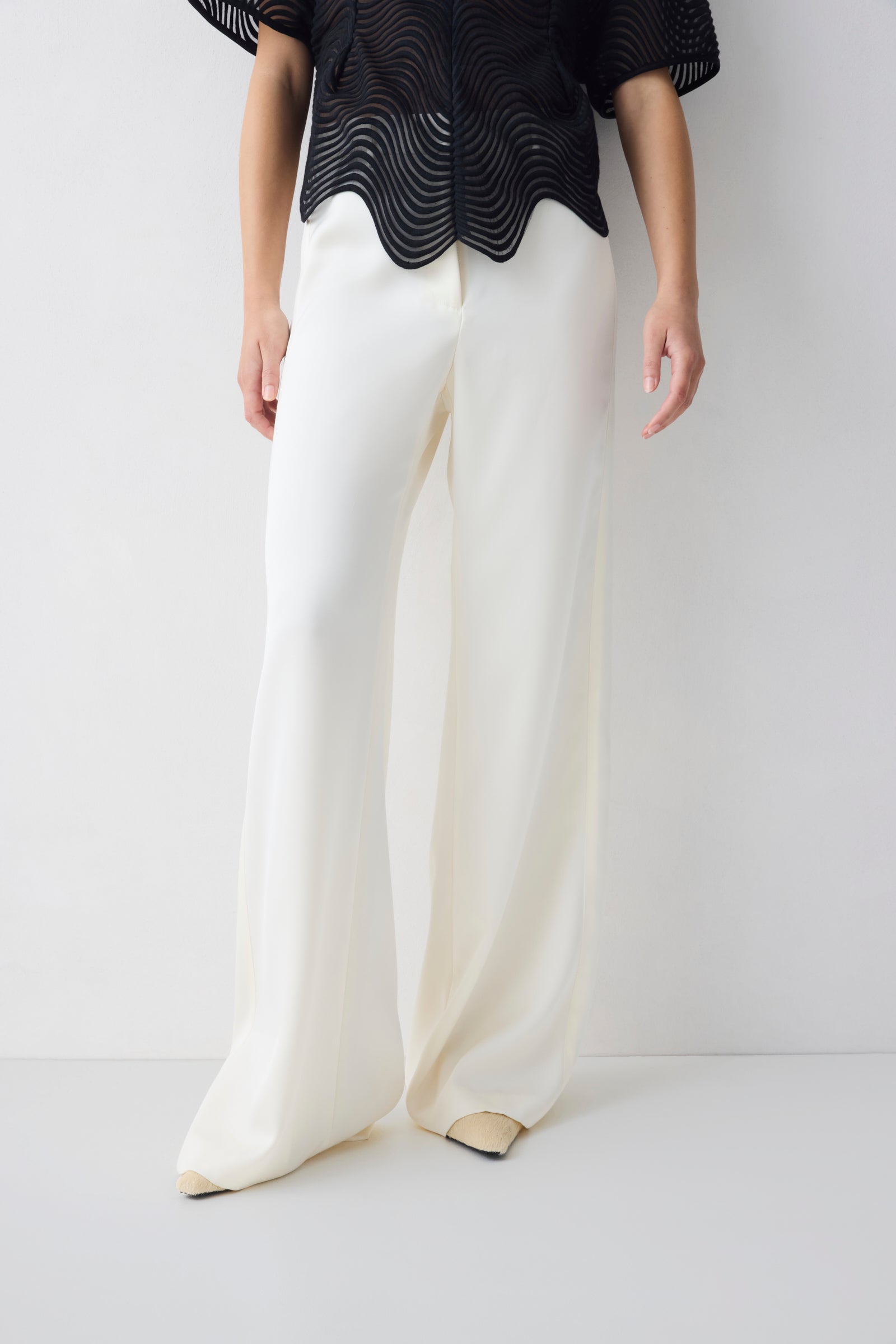 Person wearing a black top and white pants on a plain background