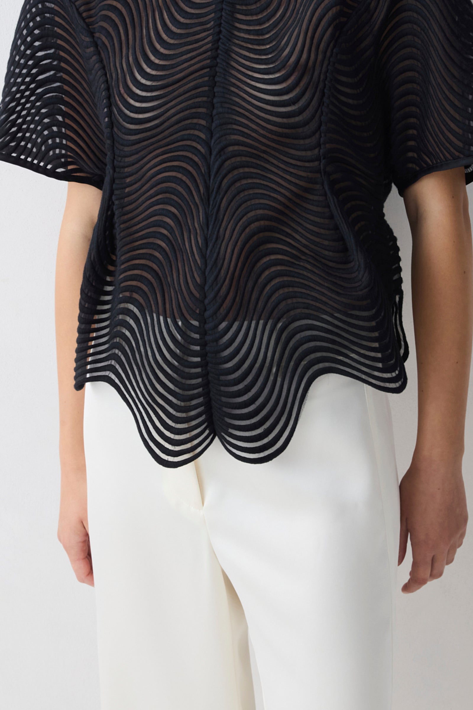 Black textured top worn by a person on a white background