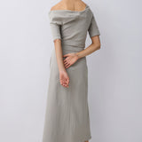 A woman modeling an off-the-shoulder top and elevated midi skirt in a light beige linen-like fabric, shown from the back against a plain light gray studio background.