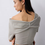 A woman shown from the back wearing a light gray off-the-shoulder linen like top and matching skirt against a plain light gray background.