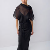 A model wearing a black sheer mesh dress with short flutter sleeves, a V-neckline, and a matching fabric tie belt at the waist, photographed against a plain light gray studio background.