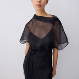 A model wearing a black midi dress with a sheer mesh yoke and flutter sleeves, standing against a light gray studio background.