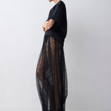 Woman wearing a black outfit with sheer overlay on a white background