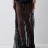 Person wearing a black top and sheer, patterned long skirt on a white background