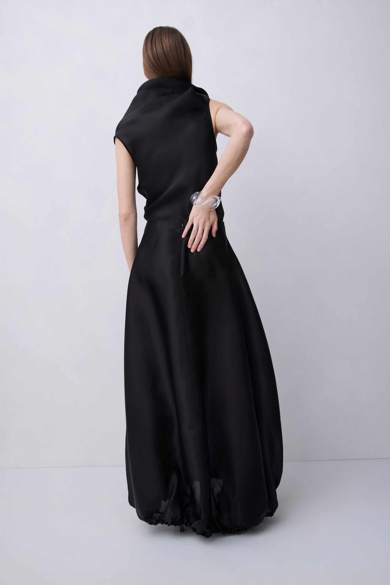 A woman wearing a sleeveless black maxi dress, shown from the back against a light gray studio background.