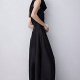 A woman modeling a sleeveless black maxi dress with a draped, voluminous skirt, photographed against a plain light gray studio background.