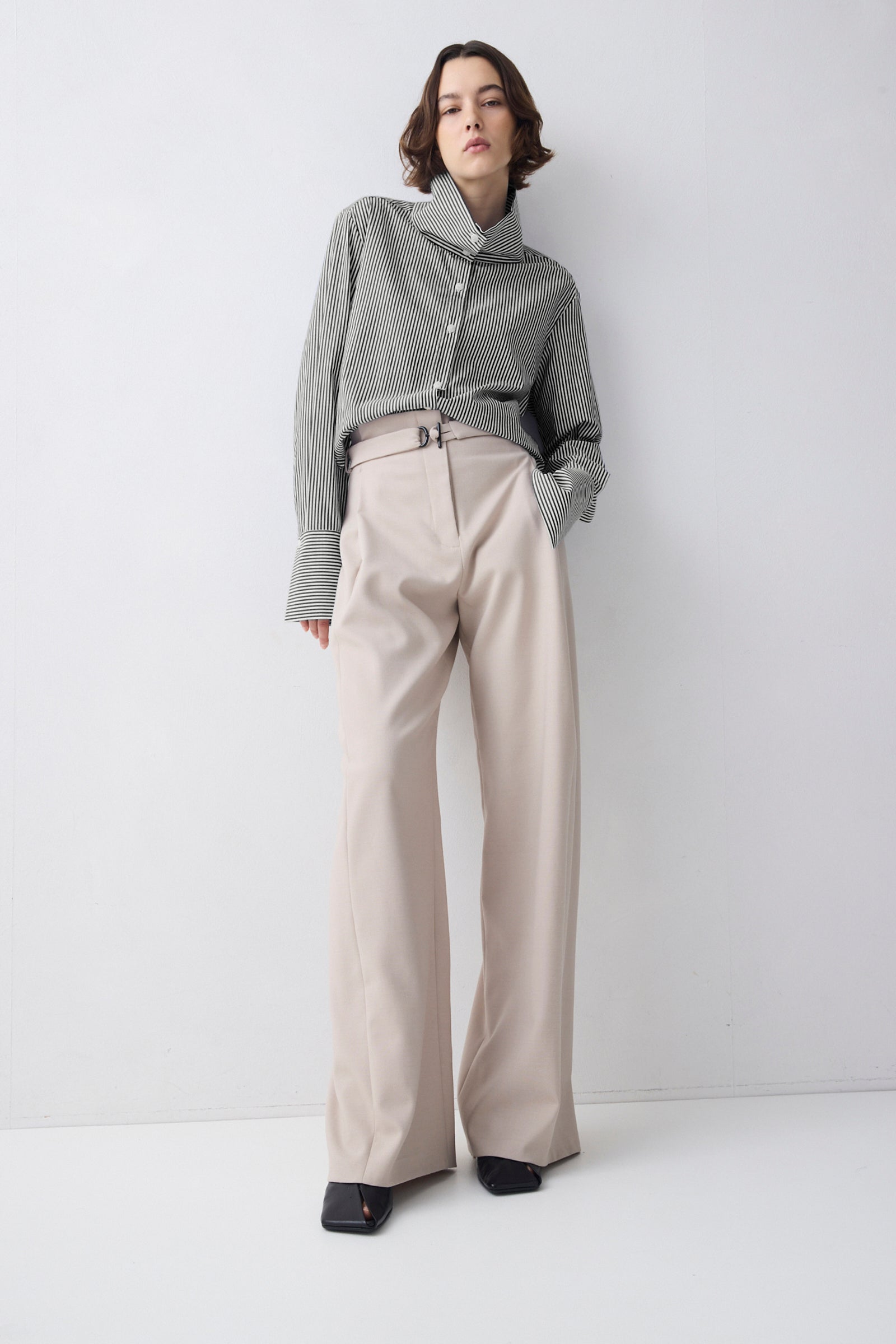 Woman wearing a gray textured shirt and beige wide-leg pants against a white background