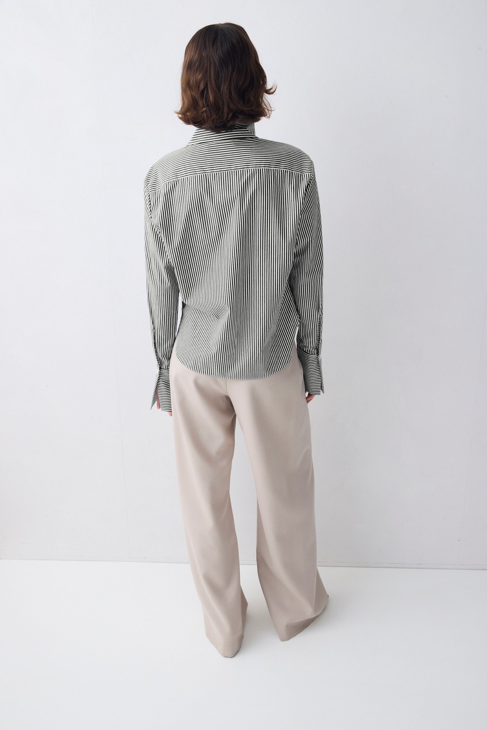Person wearing a striped shirt and beige pants on a white background
