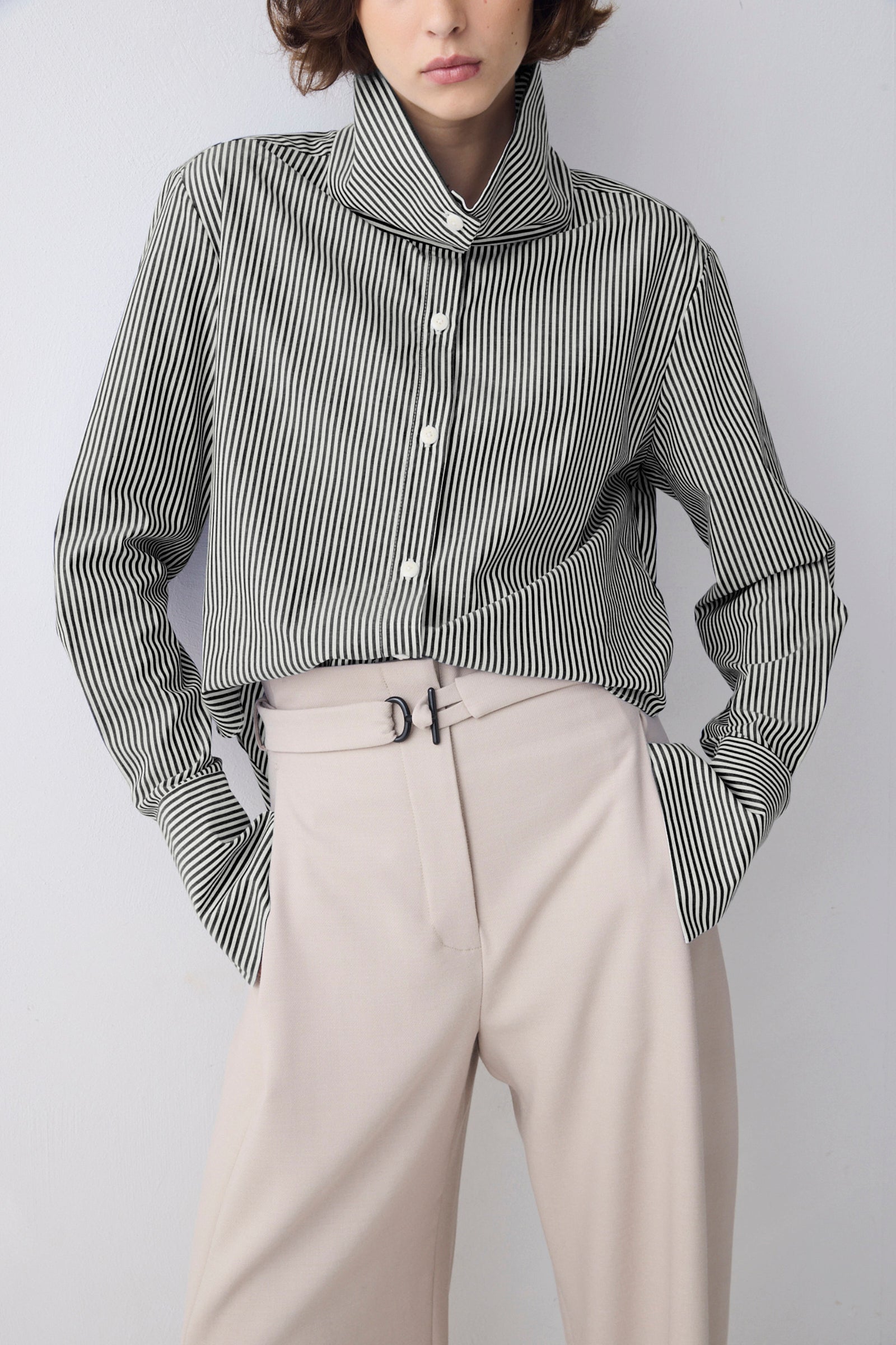 Person wearing a striped shirt and beige pants against a plain background