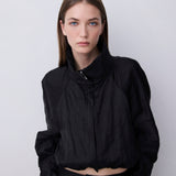 A model wearing a black cropped lightweight jacket with a high collar and front zipper, paired with black pants, set against a plain light gray studio background.
