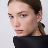 A close-up portrait of a woman with brown hair pulled back, wearing a black high-neck top against a light gray background.