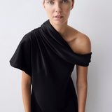 A model wearing a black draped one-shoulder dress against a light gray background.