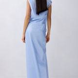 A woman with long dark hair is shown from the back wearing a sleeveless light blue maxi dress against a plain light gray studio background.