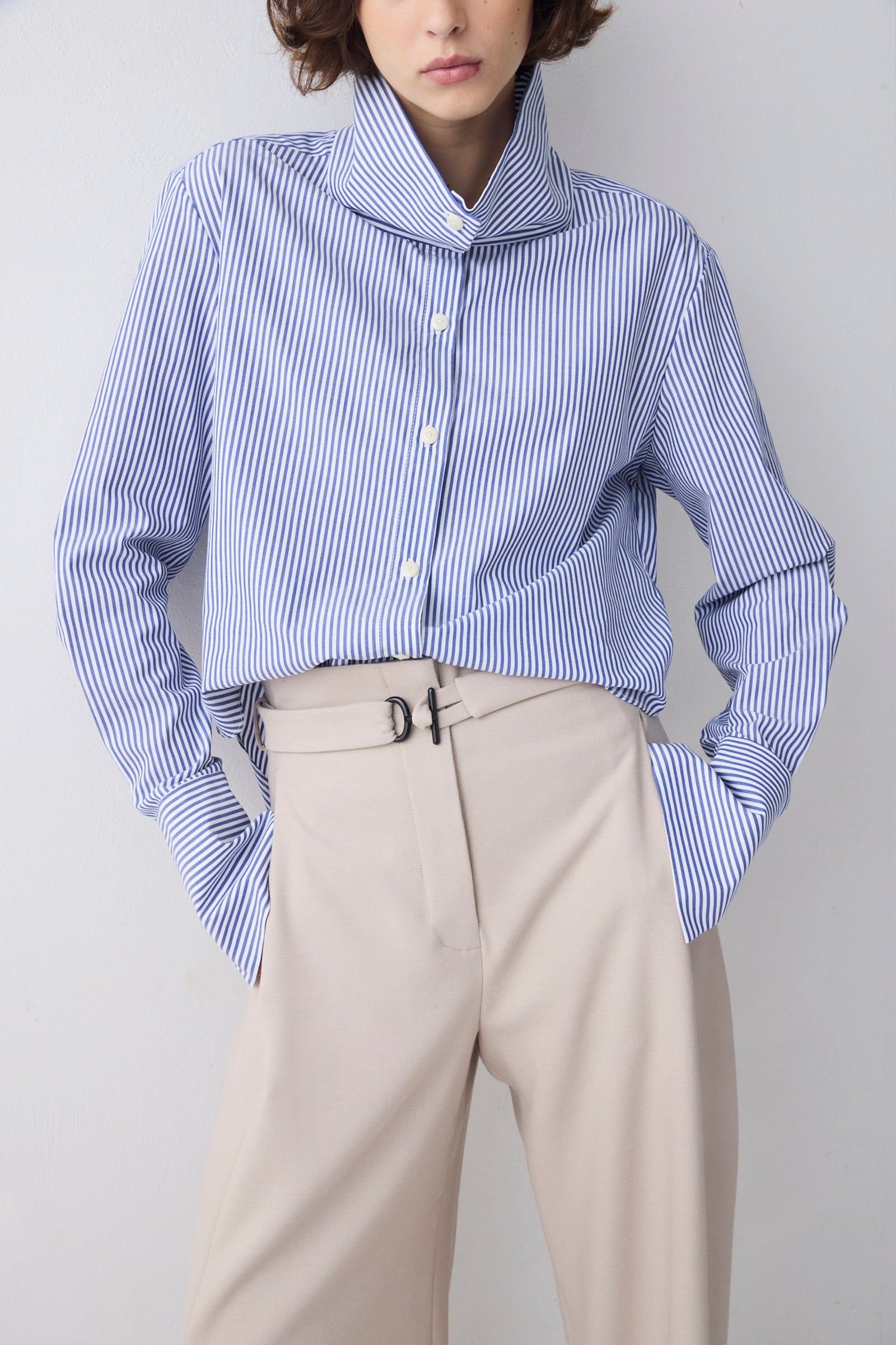 Person wearing a blue and white striped shirt with beige pants on a plain background