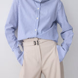 Person wearing a blue and white striped shirt with beige pants on a plain background