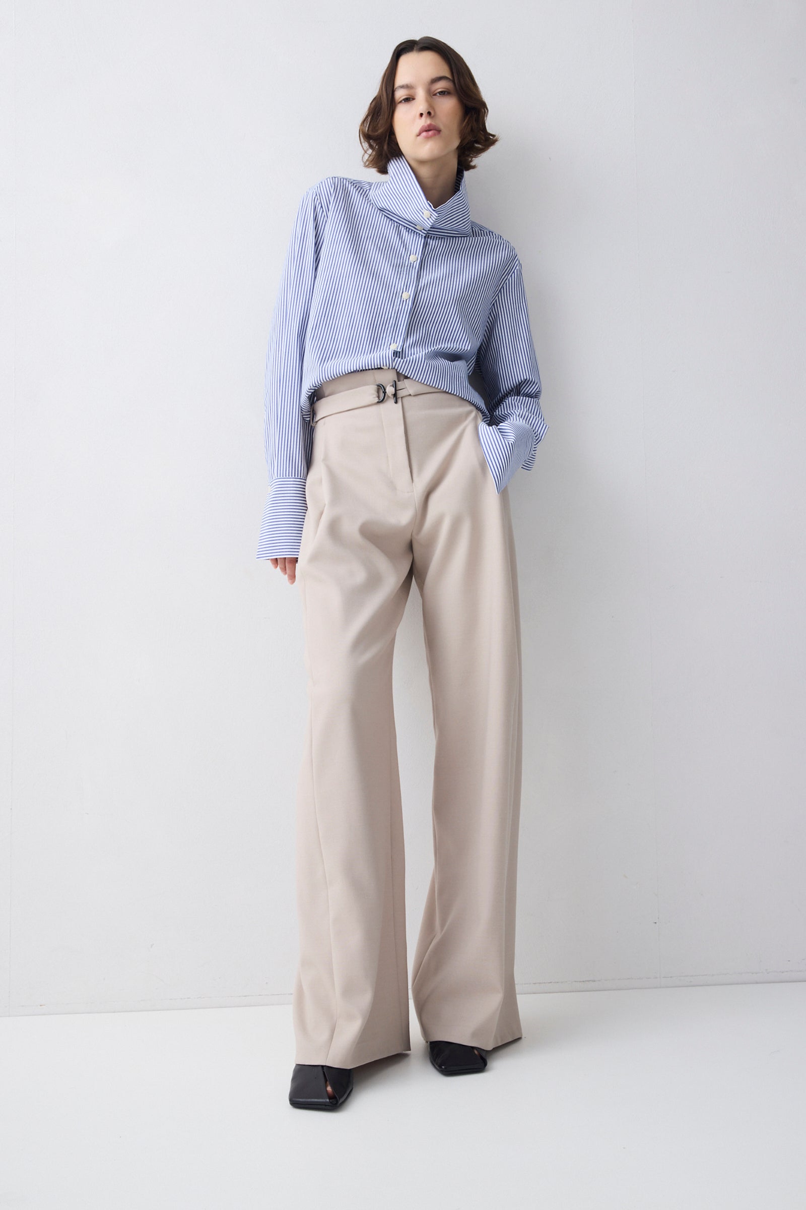 Person wearing a light blue blouse and beige pants on a white background