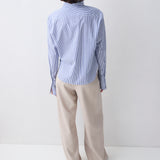 Person wearing a light blue striped shirt and beige pants on a white background