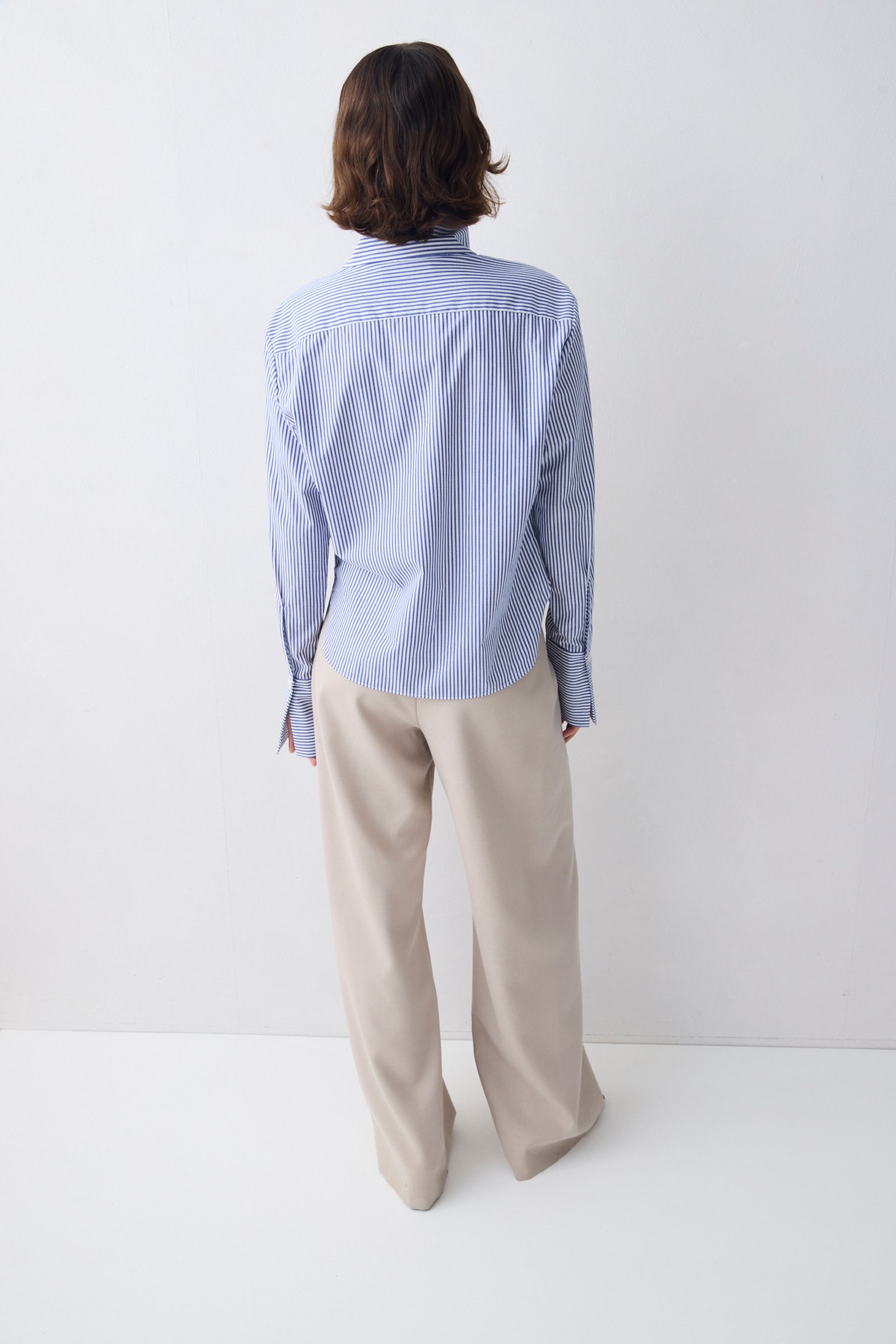 Person wearing a light blue striped shirt and beige pants on a white background