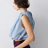 Woman wearing a light blue sleeveless top and dark purple pants against a plain background