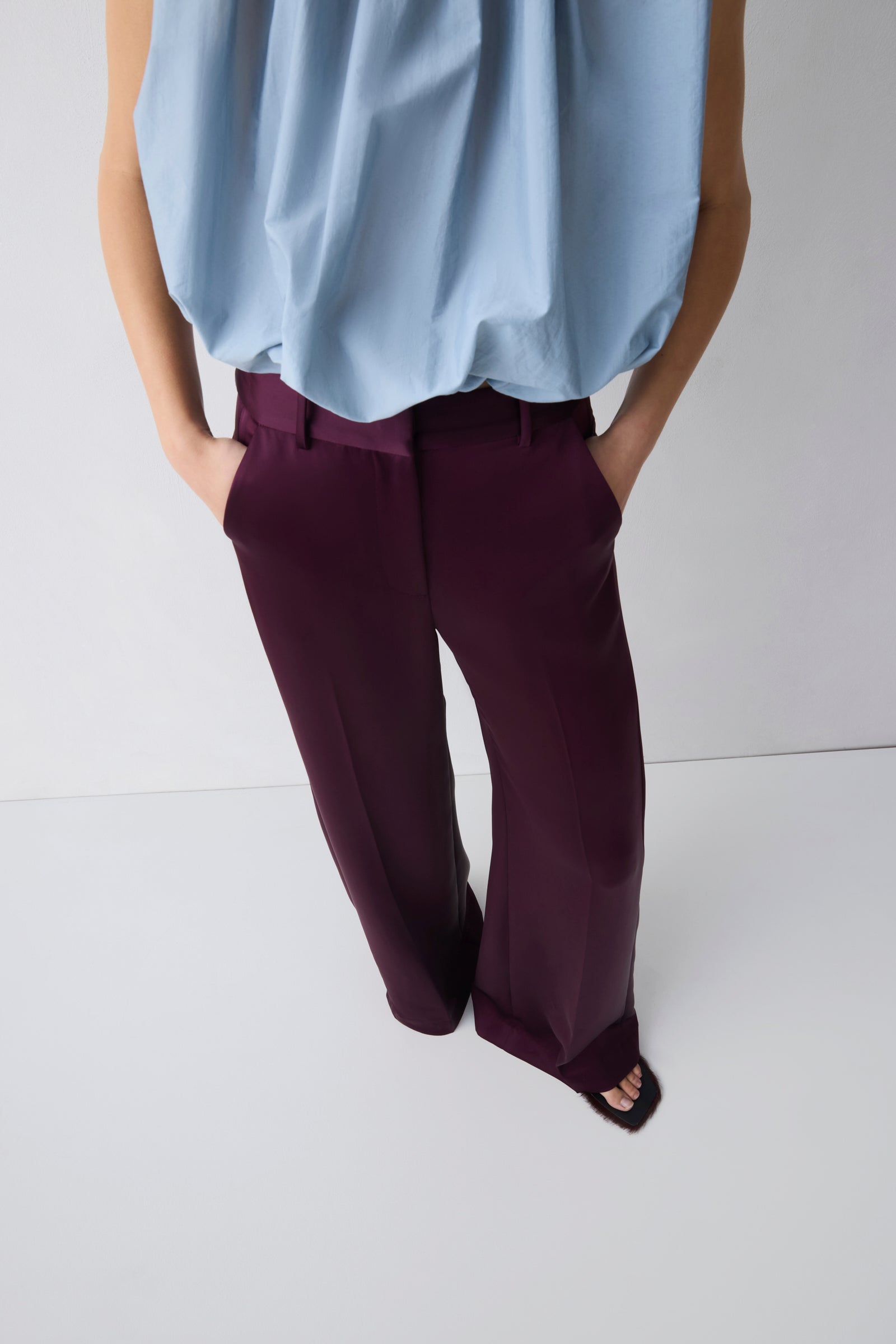 Person wearing a light blue shirt and dark purple pants on a white background
