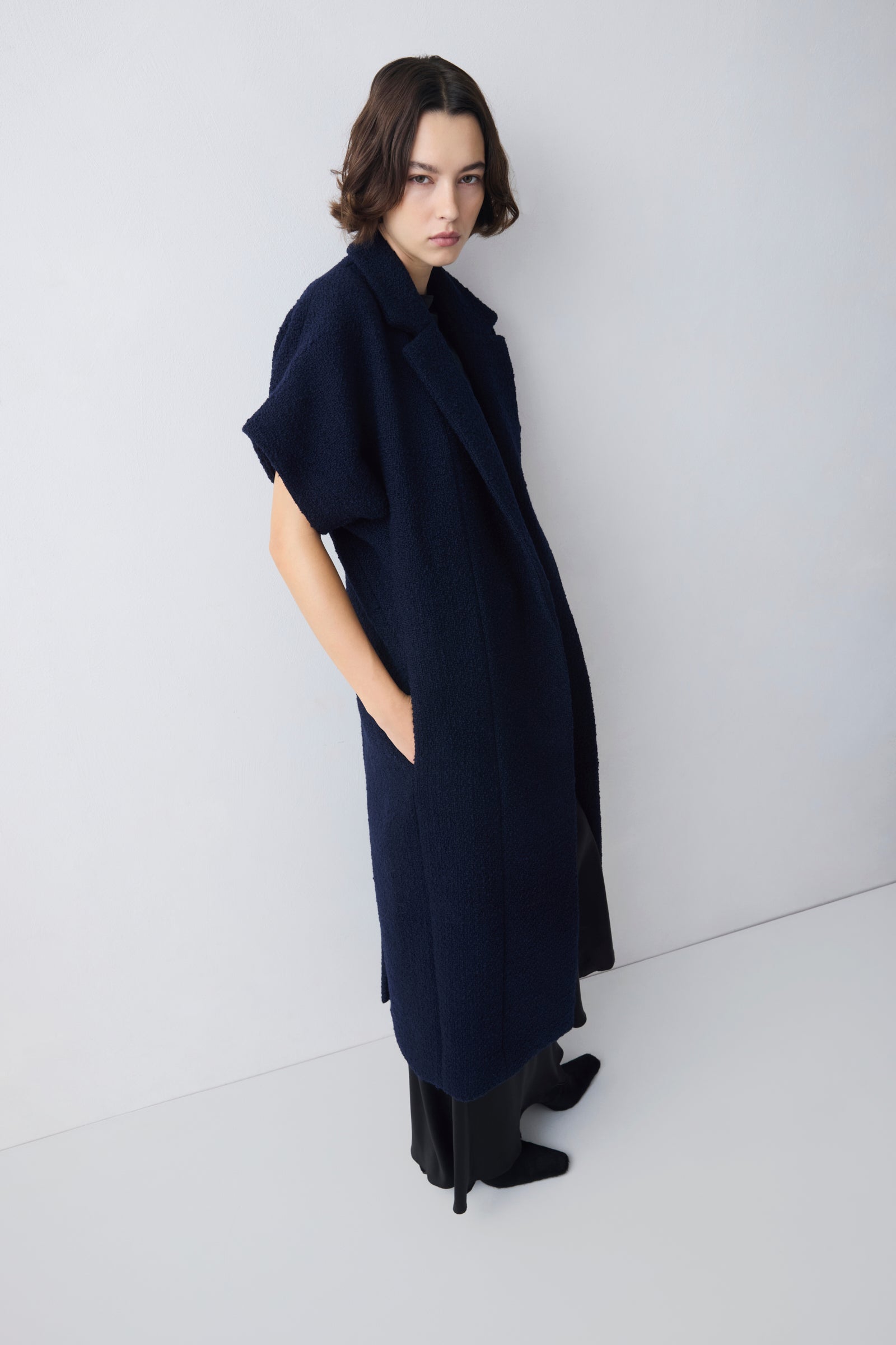 Person wearing a long navy coat against a white background