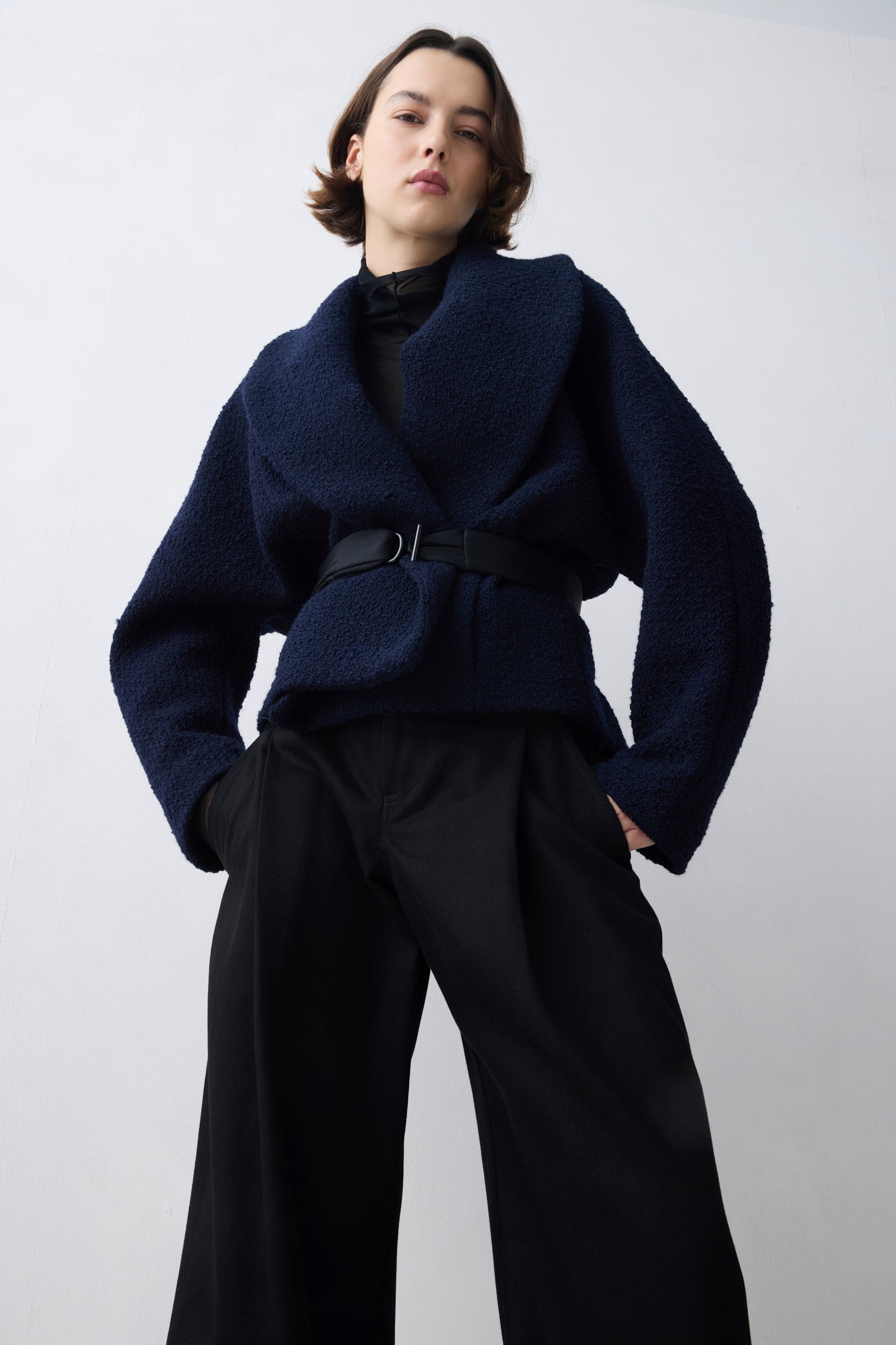 Person wearing a dark blue jacket and black pants on a white background