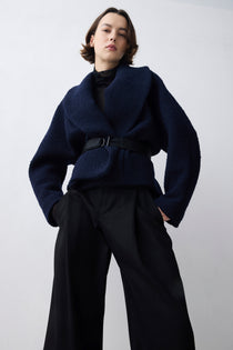 Person wearing a dark blue jacket and black pants on a white background