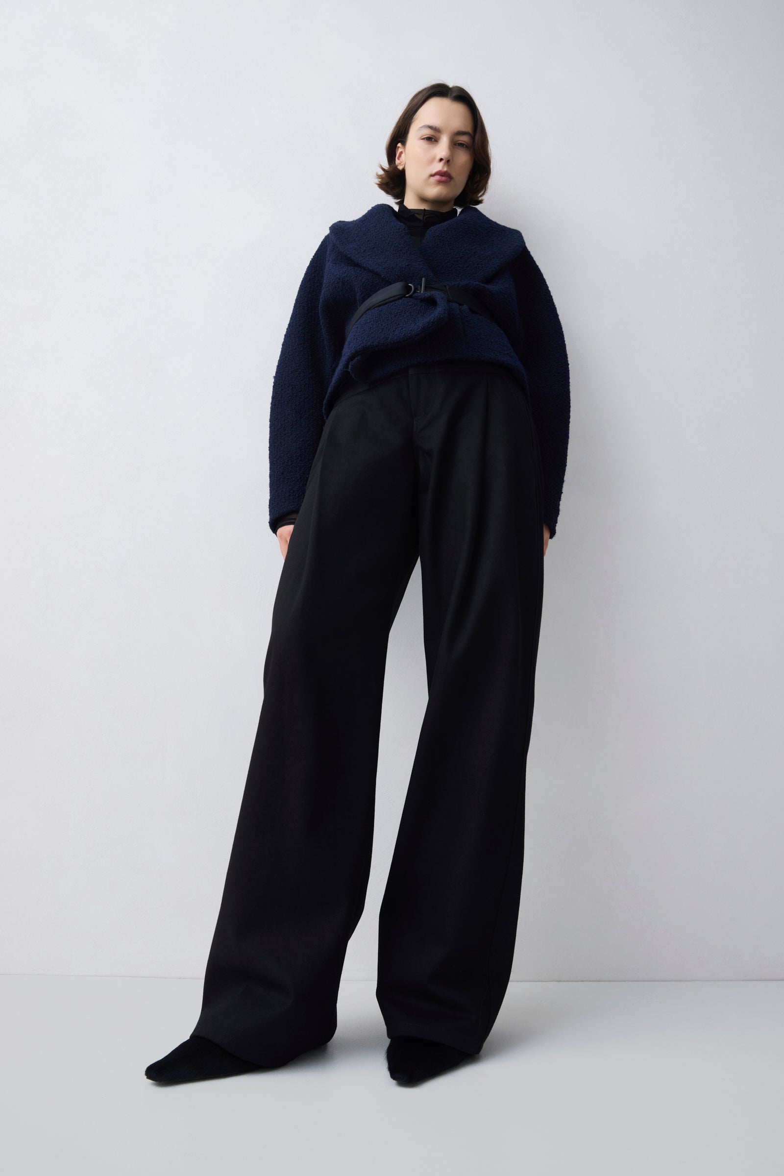 Person wearing a navy blue jacket and black pants on a white background