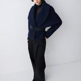Person wearing a navy blue jacket and black pants against a white background