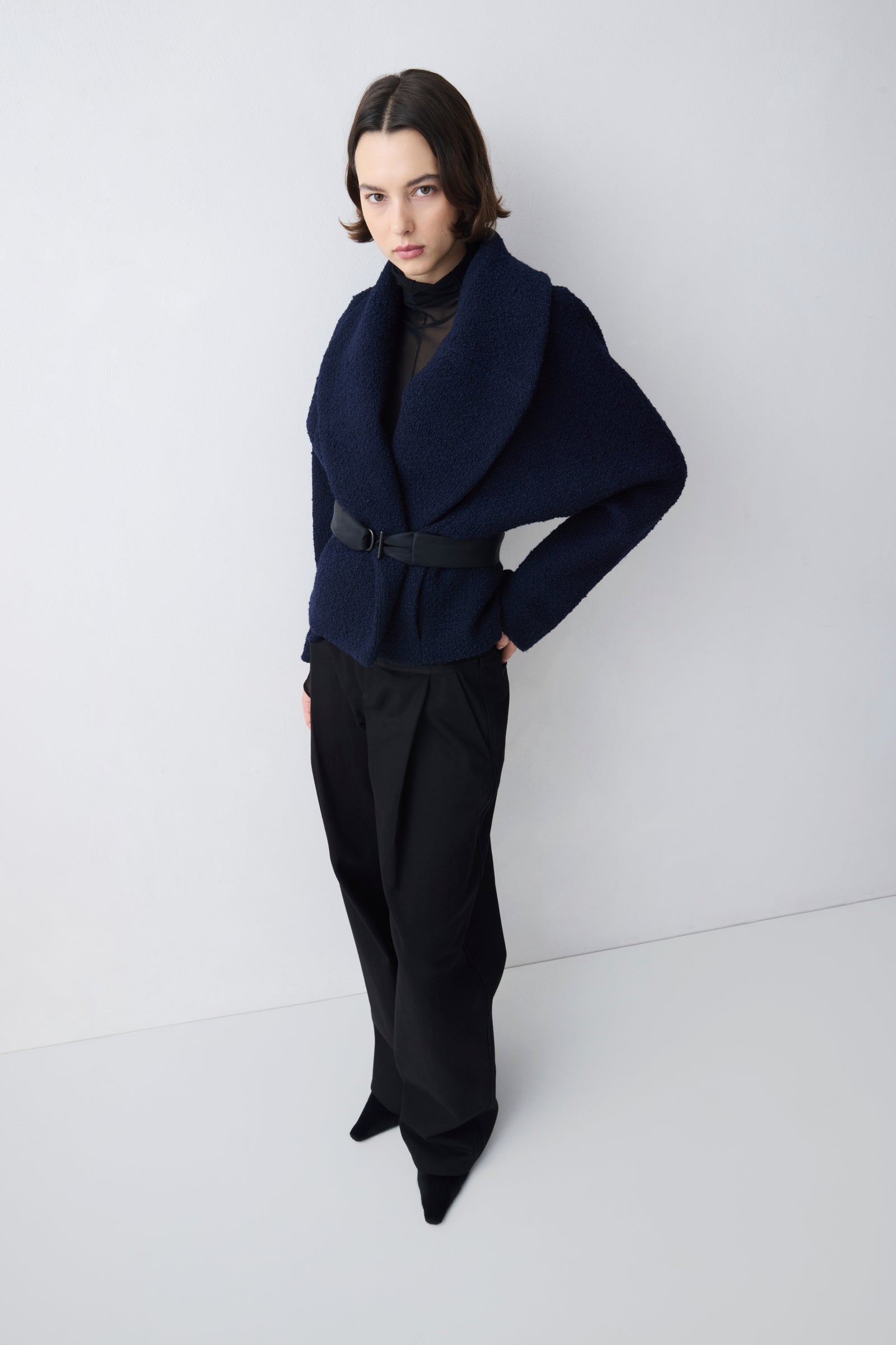 Person wearing a navy blue jacket and black pants against a white background