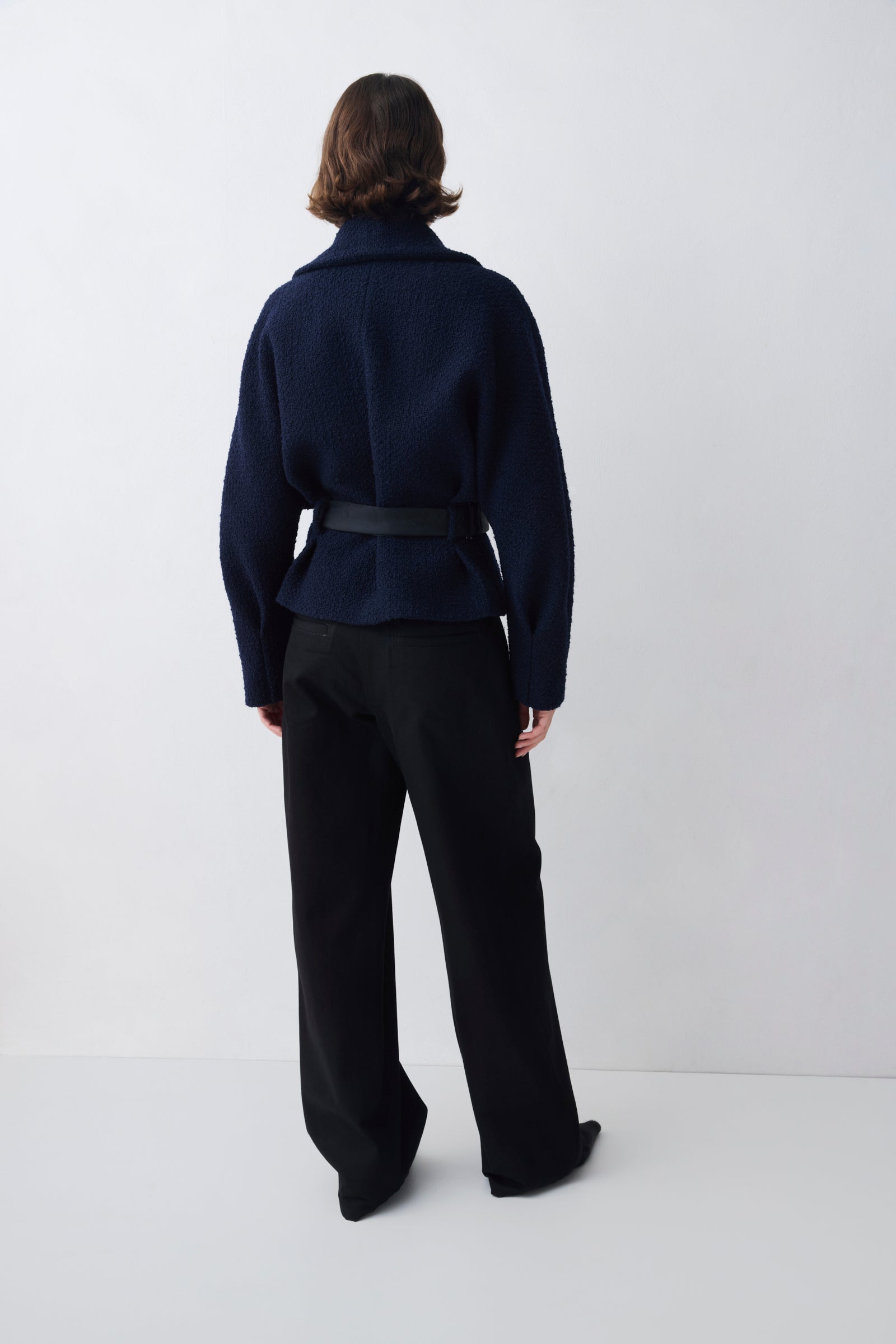 Person wearing a dark blue jacket and black pants on a white background
