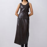 A model wearing a dark gray faux-leather sleeveless top and matching skirt set, paired with black boots, against a light gray studio background.