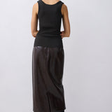 A model shown from the back wearing a black sleeveless top and a black textured midi skirt, paired with black heeled boots, against a light gray studio background.
