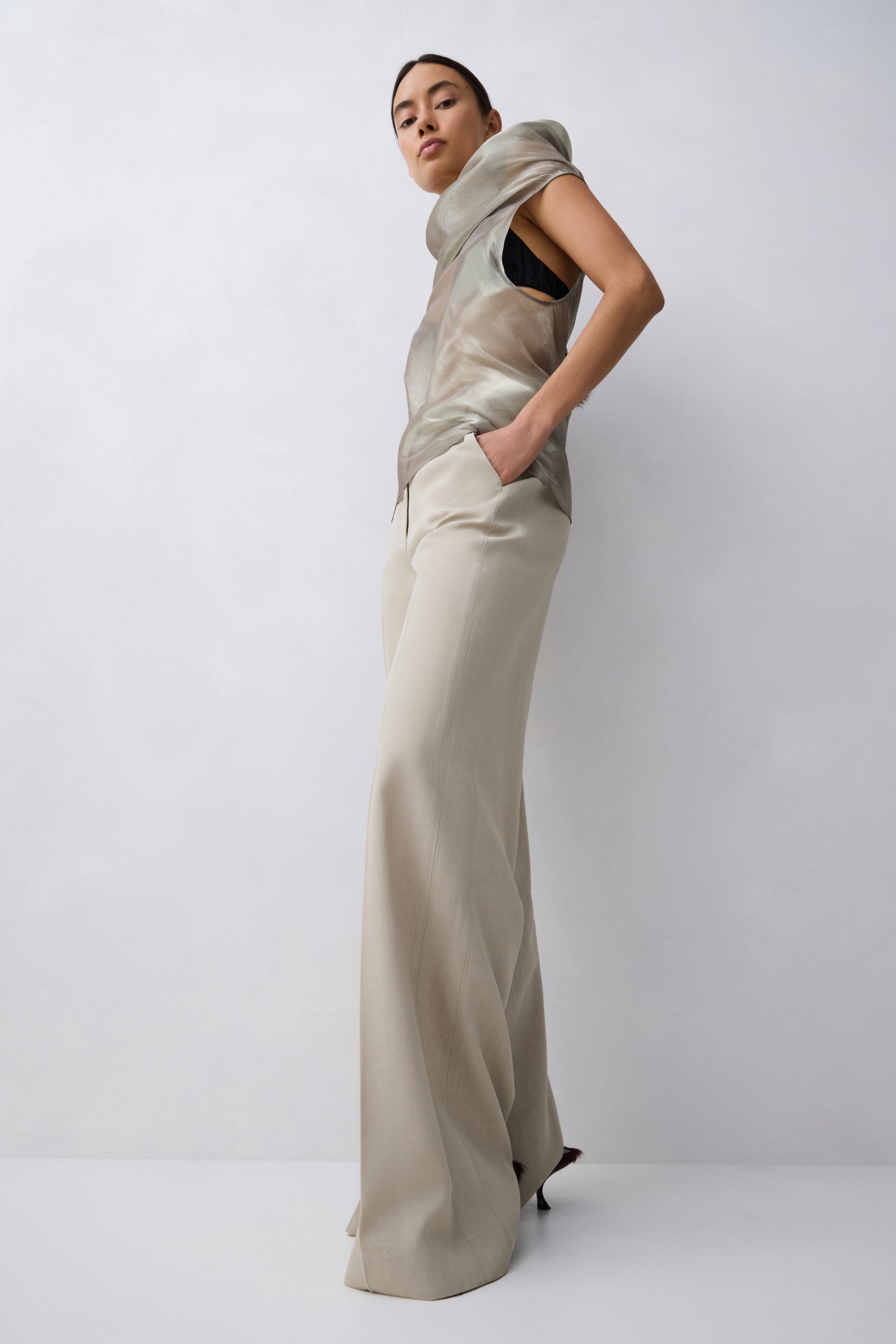A model wearing a beige satin-like draped top and matching wide-leg trousers, posing against a light gray studio background.
